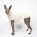 Whippet dog wearing a fluffy reversible sleeveless sweater/jumper in vanilla/white colour standing left side on